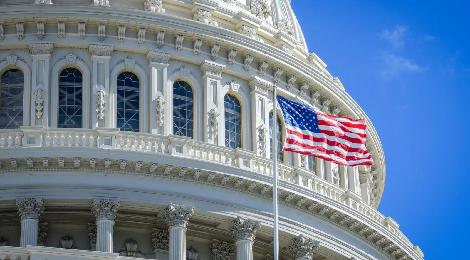 The U.S. Capitol dome and the American flag against a blue sky
